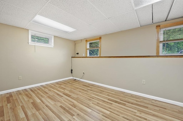 below grade area featuring light wood-style floors, baseboards, and a drop ceiling