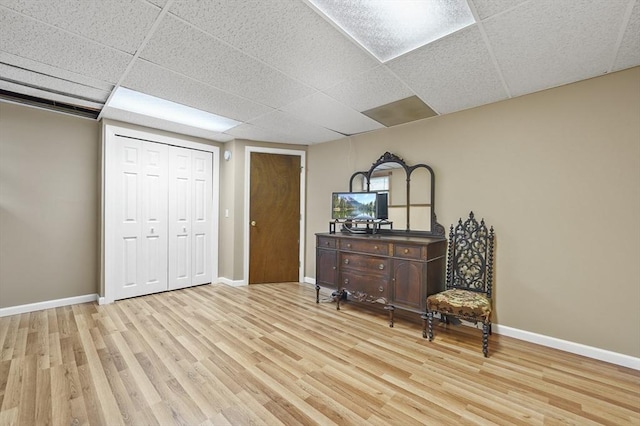 bedroom with wood finished floors, baseboards, a drop ceiling, and a closet