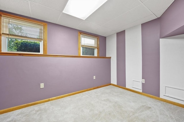 carpeted spare room with a drop ceiling and baseboards