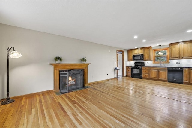 unfurnished living room featuring light wood-type flooring, a sink, recessed lighting, and baseboards