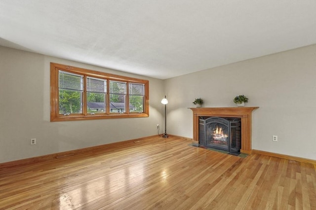 unfurnished living room featuring a fireplace with flush hearth, wood finished floors, and baseboards