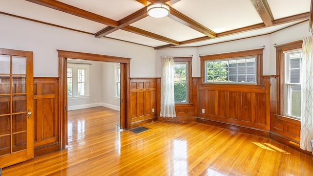 interior space featuring beam ceiling, a wainscoted wall, coffered ceiling, and light wood-style floors