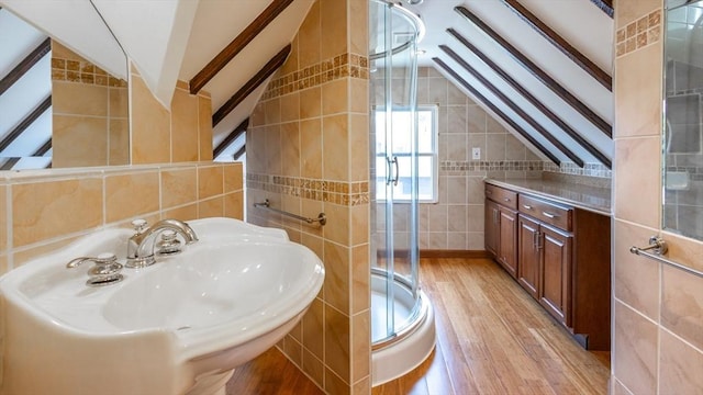 full bathroom featuring a sink, wood finished floors, tile walls, a shower stall, and lofted ceiling