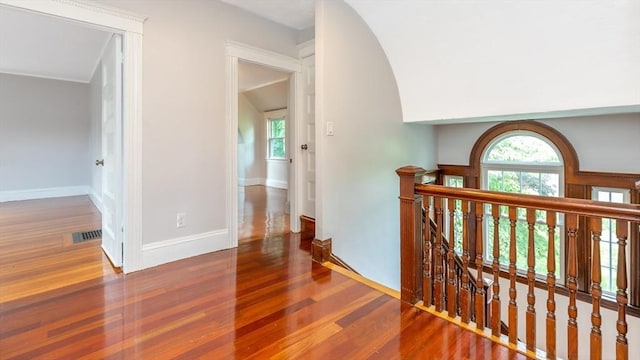 hall featuring an upstairs landing, visible vents, baseboards, and wood finished floors