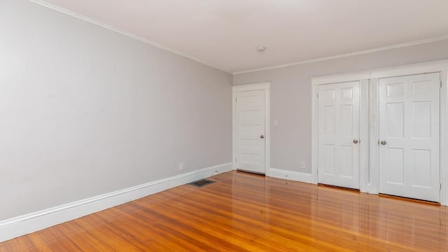 unfurnished bedroom with wood finished floors, baseboards, visible vents, a closet, and crown molding