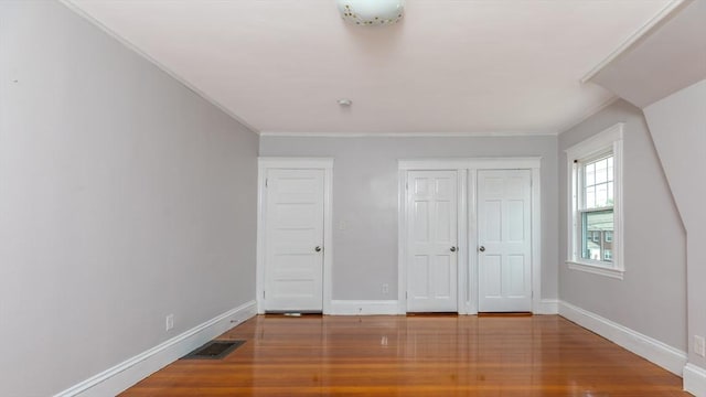 unfurnished bedroom featuring wood finished floors, visible vents, baseboards, a closet, and crown molding