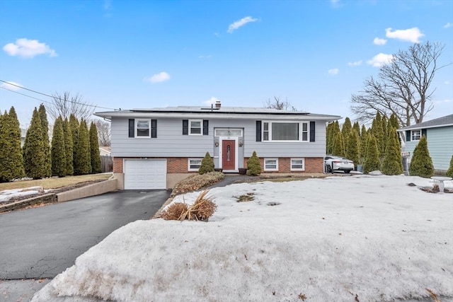 split foyer home featuring aphalt driveway, roof mounted solar panels, brick siding, and a garage