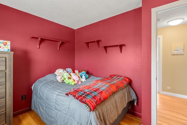 bedroom with a textured ceiling, baseboards, and wood finished floors