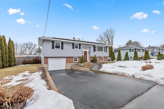 bi-level home featuring an attached garage, fence, driveway, and roof mounted solar panels