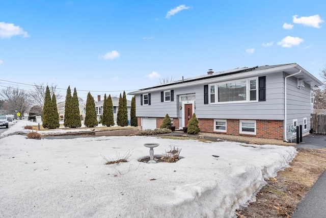 raised ranch with brick siding, roof mounted solar panels, and an attached garage