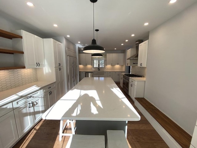 kitchen with wall chimney range hood, white cabinetry, appliances with stainless steel finishes, and a kitchen island