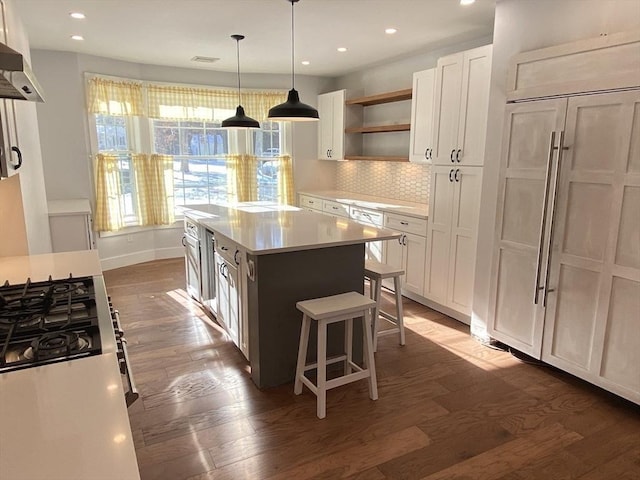 kitchen with decorative light fixtures, backsplash, range hood, a kitchen island, and white cabinets