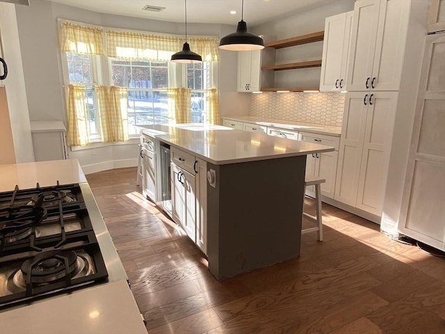 kitchen featuring dark hardwood / wood-style flooring, stovetop, pendant lighting, white cabinets, and a center island