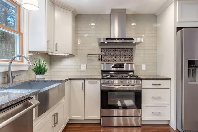 kitchen featuring dark stone countertops, stainless steel appliances, white cabinetry, wall chimney exhaust hood, and a sink