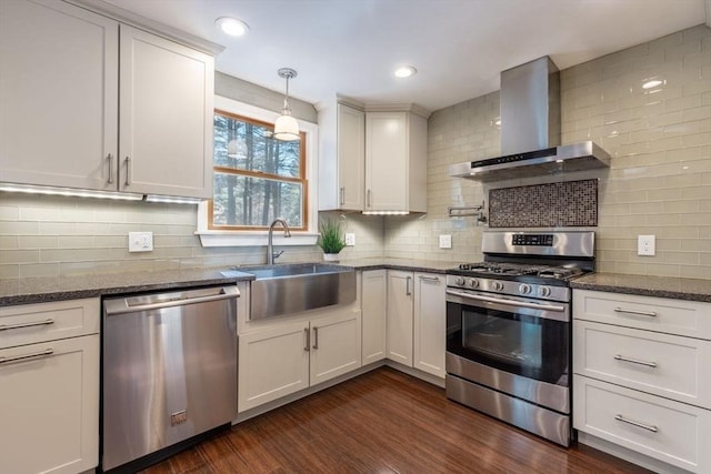 kitchen with a sink, dark wood-style floors, stainless steel appliances, dark stone counters, and wall chimney exhaust hood