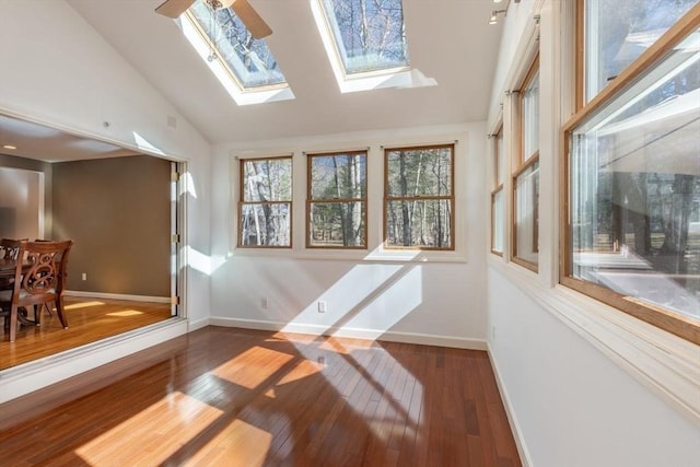 interior space featuring vaulted ceiling with skylight, baseboards, and hardwood / wood-style floors