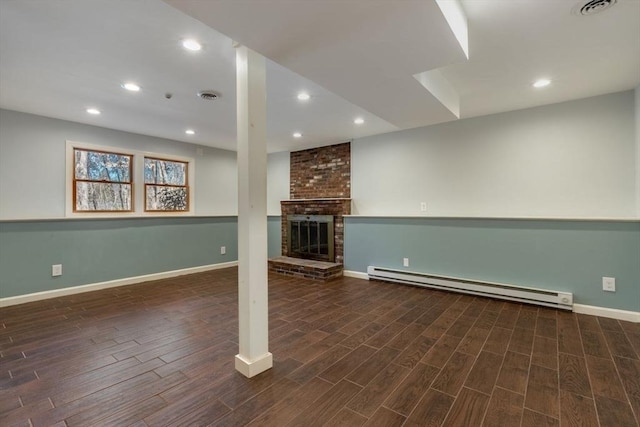 basement featuring dark wood-style floors, visible vents, recessed lighting, a brick fireplace, and baseboard heating