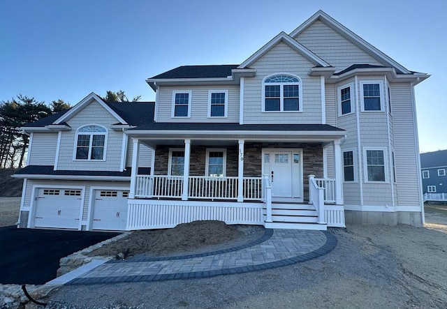 view of front of house with a garage, driveway, stone siding, and covered porch