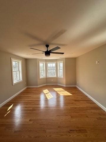 unfurnished room featuring ceiling fan, a wealth of natural light, wood finished floors, and baseboards