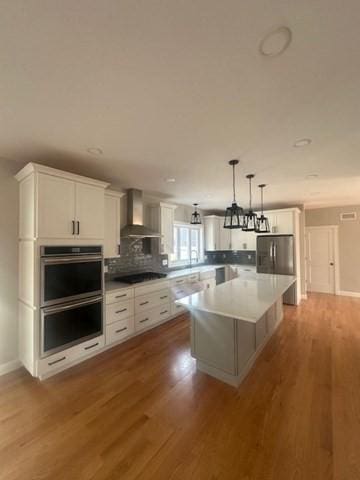 kitchen with white cabinets, a kitchen island, wall chimney range hood, and appliances with stainless steel finishes