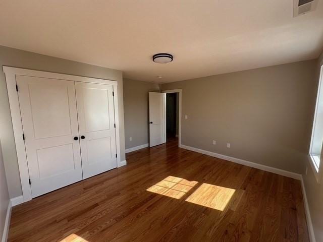 unfurnished bedroom featuring baseboards, wood finished floors, visible vents, and a closet