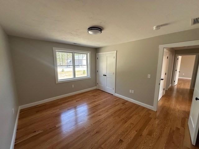 unfurnished bedroom featuring wood finished floors, a closet, baseboards, and visible vents