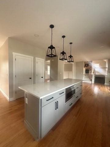 kitchen with hanging light fixtures, light wood-type flooring, light countertops, baseboards, and a kitchen island
