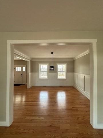 unfurnished dining area featuring wainscoting, wood finished floors, a decorative wall, and crown molding
