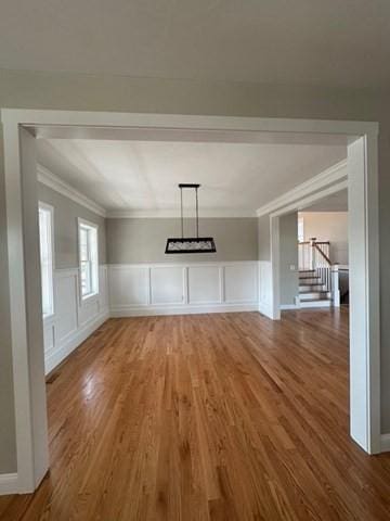 unfurnished dining area with stairs, crown molding, wood finished floors, and a decorative wall
