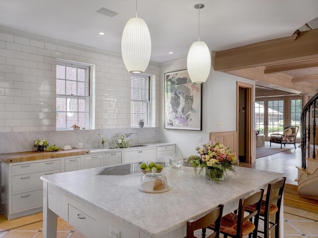 kitchen featuring black electric cooktop, white cabinetry, backsplash, and hanging light fixtures