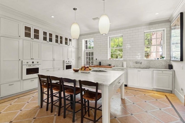 kitchen with a center island, hanging light fixtures, oven, a breakfast bar, and light tile patterned floors