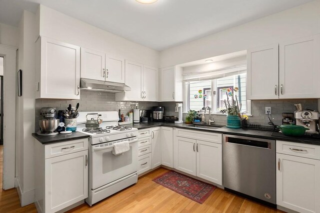 kitchen featuring dishwasher, white gas range, under cabinet range hood, a sink, and dark countertops