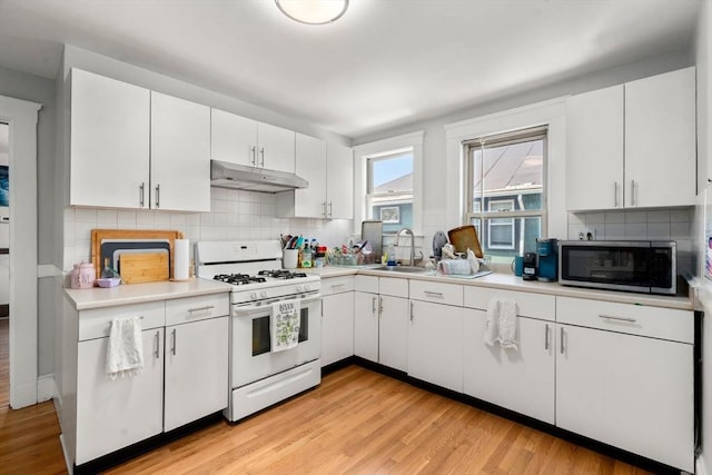 kitchen with white gas stove, stainless steel microwave, under cabinet range hood, a sink, and light countertops