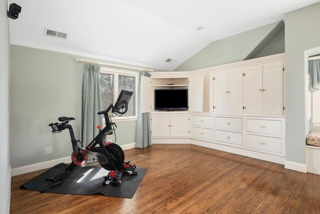 exercise room with visible vents, baseboards, wood finished floors, and vaulted ceiling