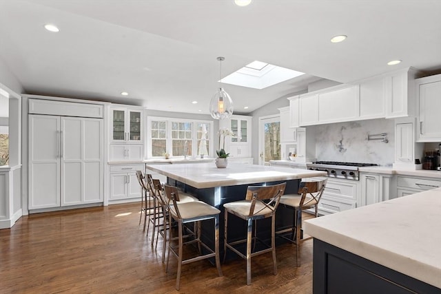 kitchen featuring stainless steel appliances, vaulted ceiling with skylight, glass insert cabinets, and white cabinetry