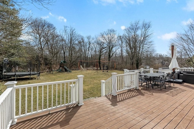 wooden terrace with a yard, a trampoline, outdoor dining space, and a playground