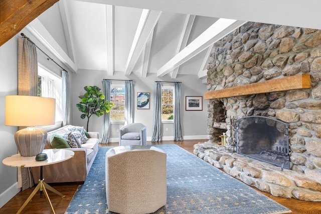 living area featuring a stone fireplace, lofted ceiling with beams, baseboards, and wood finished floors