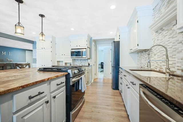 kitchen featuring stainless steel appliances, a sink, white cabinets, dark stone countertops, and decorative light fixtures