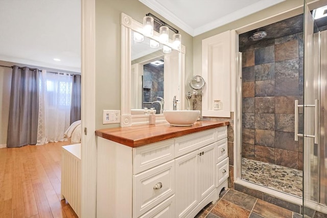 bathroom with connected bathroom, wood finished floors, vanity, a shower stall, and crown molding