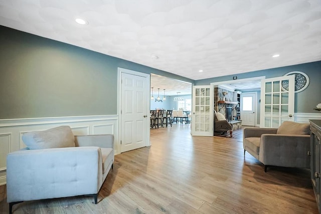 living area featuring french doors, wainscoting, light wood-style flooring, and a decorative wall