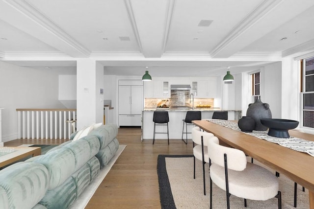 dining space with beam ceiling, dark wood-type flooring, sink, and ornamental molding