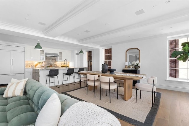 interior space with light wood-type flooring, ornamental molding, sink, and beamed ceiling