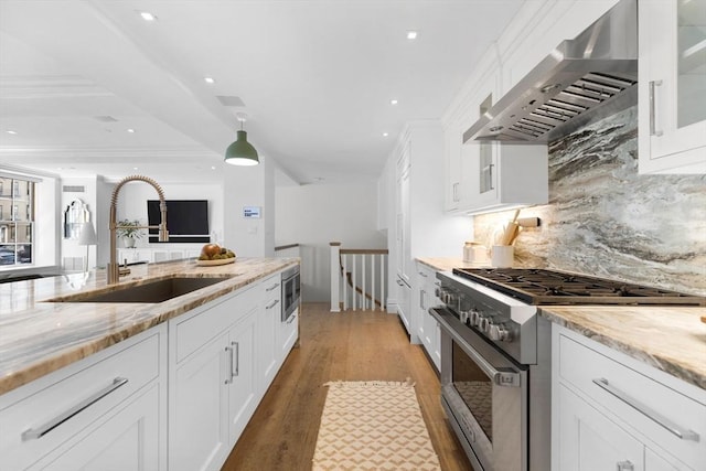 kitchen featuring appliances with stainless steel finishes, white cabinetry, wall chimney range hood, decorative backsplash, and light stone counters