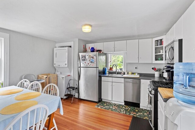 28 Gardner St, Arlington, MA 02474 - kitchen with stainless steel appliances, stacked washer and clothes dryer, a sink, and white cabinetry