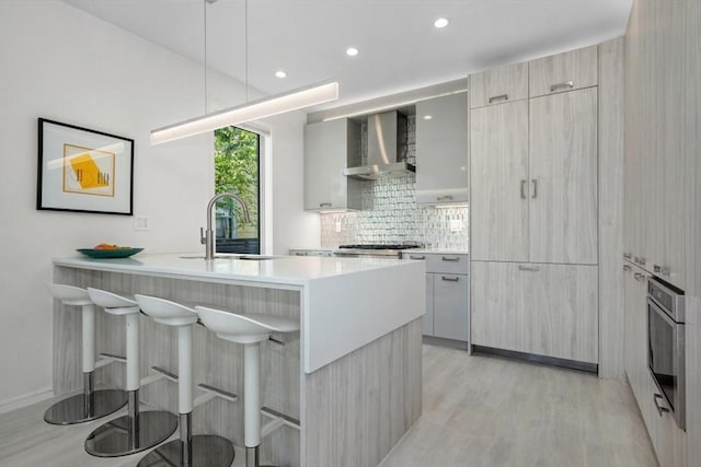 62 Pearl Unit 62, Cambridge, MA 02139 - kitchen with wall chimney range hood, a sink, modern cabinets, a breakfast bar, and light wood-style flooring