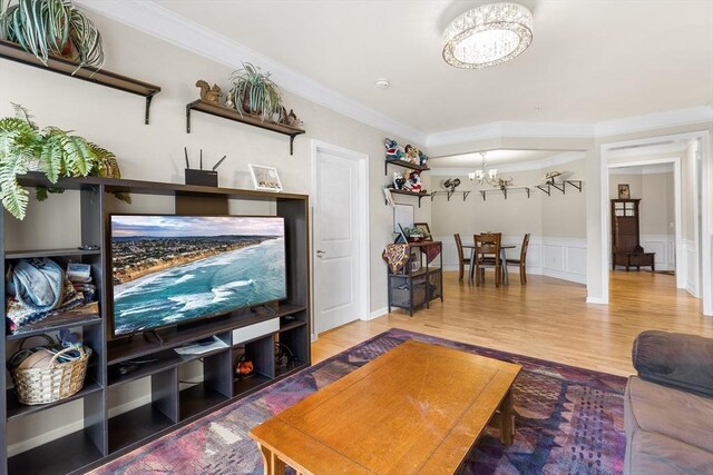 living room with wood-type flooring, ornamental molding, and a notable chandelier