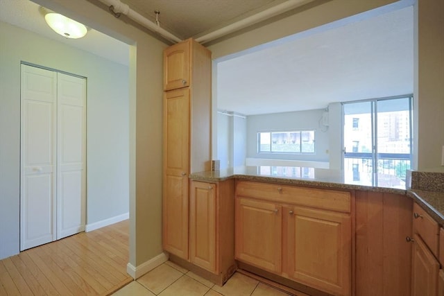872 Massachusetts Ave Unit 401, Cambridge, MA 02139 - kitchen with stone counters, a peninsula, light brown cabinets, and light tile patterned floors