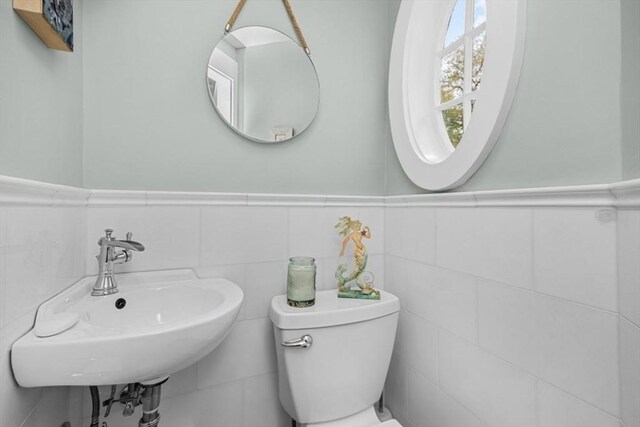 half bath featuring a sink, wainscoting, toilet, and tile walls