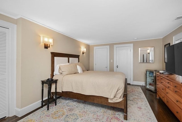 bedroom featuring dark wood finished floors, baseboards, crown molding, and two closets