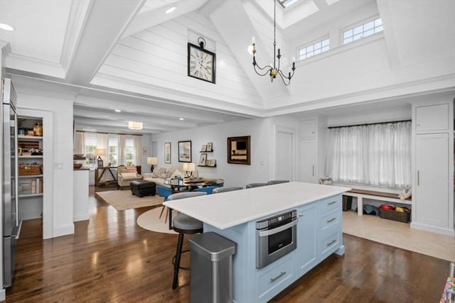 kitchen featuring stainless steel appliances, a kitchen island, dark wood-type flooring, light countertops, and beam ceiling